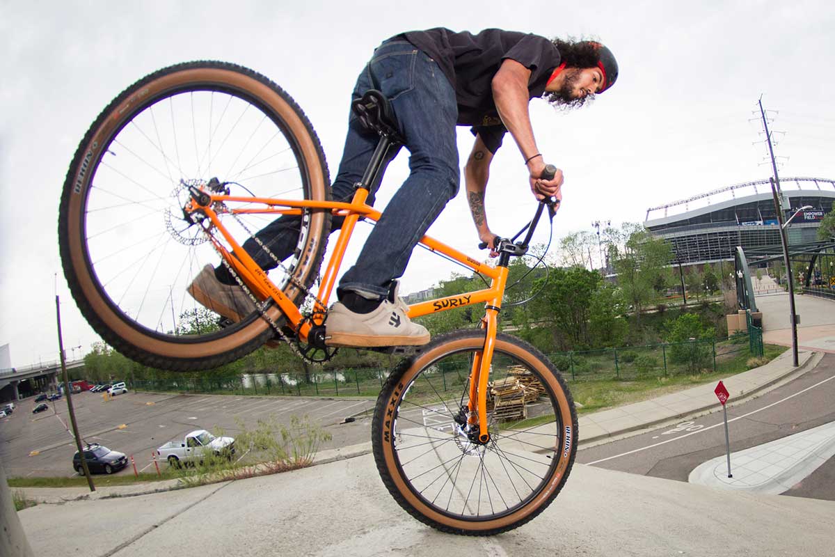 Biker wearing helmet and jeans riding Surly Lowside riding and using front brake to lift rear wheel off ground balancing on front wheel