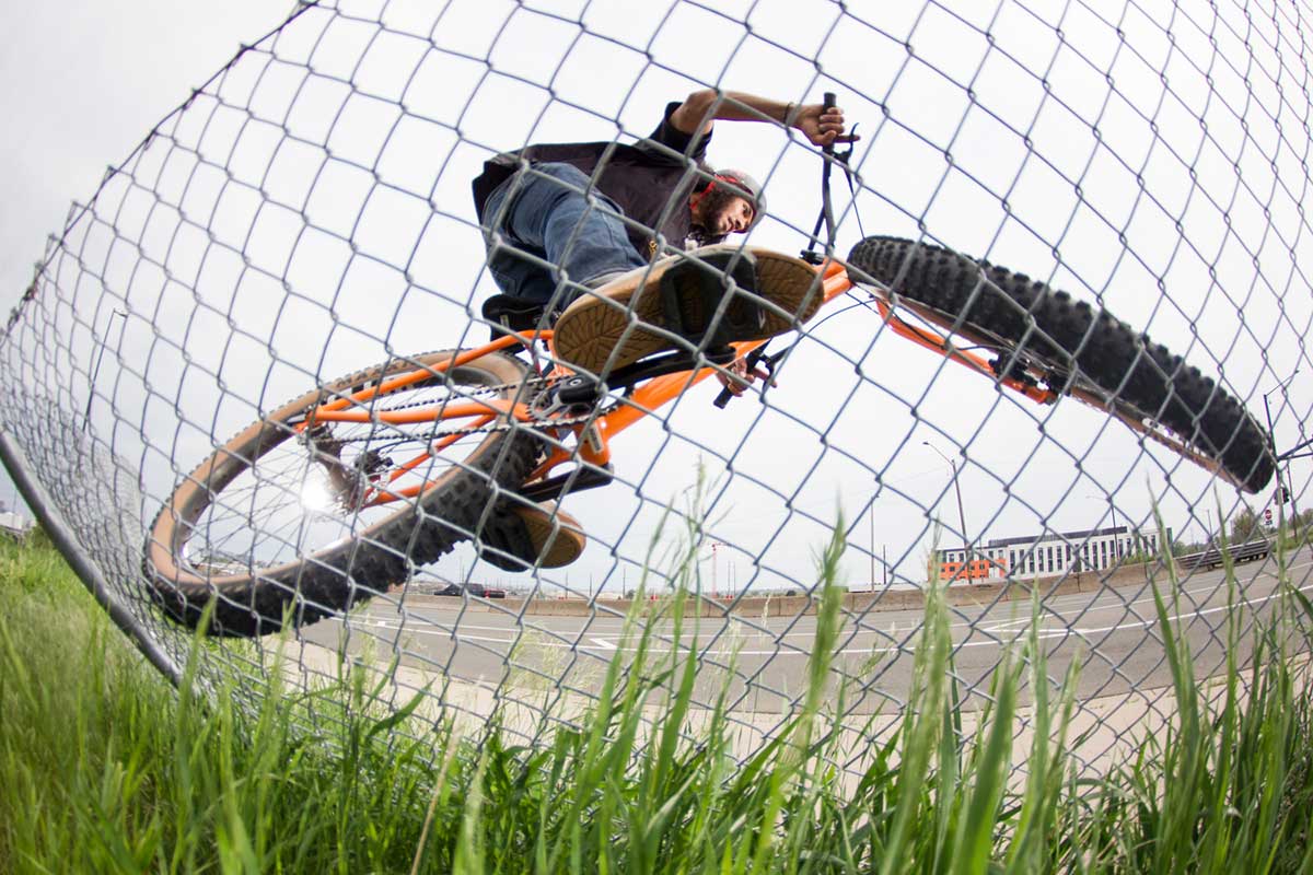 Biker wearing helmet and jeans riding Surly Lowside off of chain link fence