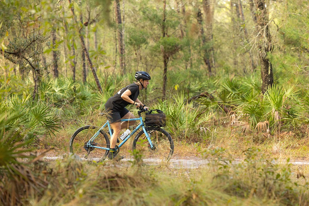 Person riding Preamble Flat Bar bike on gravel road through forest