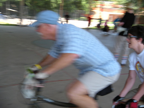 Left side, seat up view of a cyclist, on a Surly Big Dummy bike with a person on back, during a race on an outdoor court