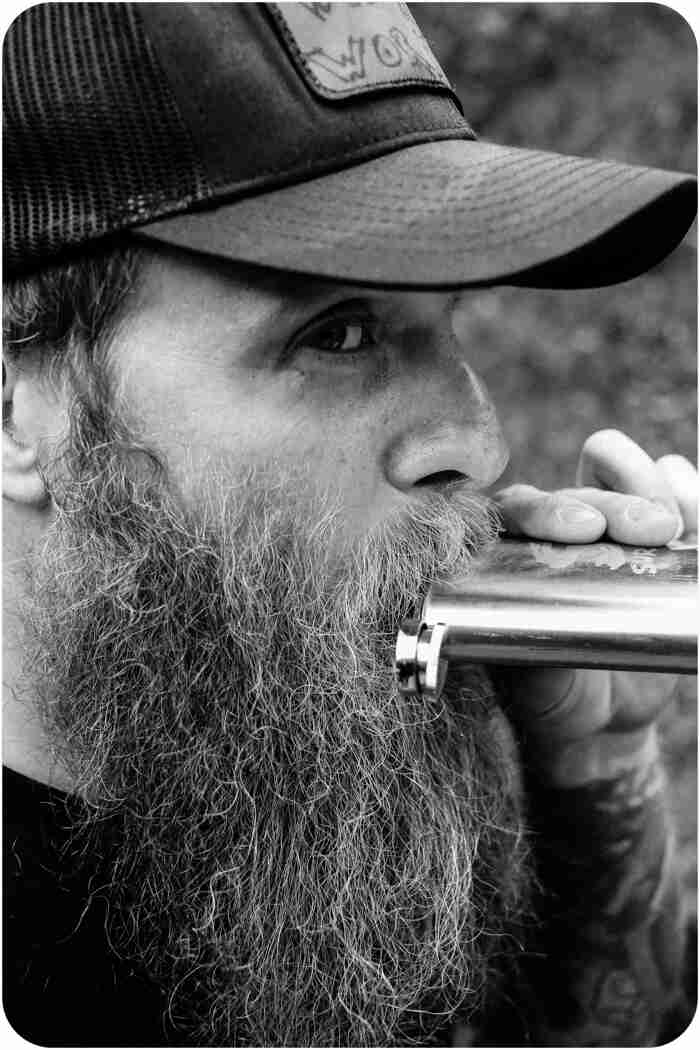 Right side headshot of a person with a beard, drinking from a flask - black & white image