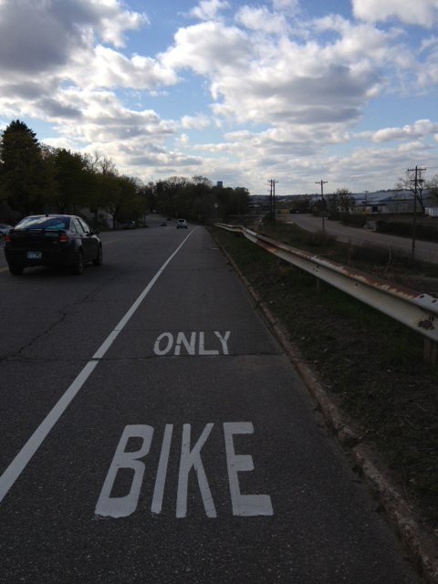 Straight away view of a paved bike lane on the right side of a roadway with cars next to it
