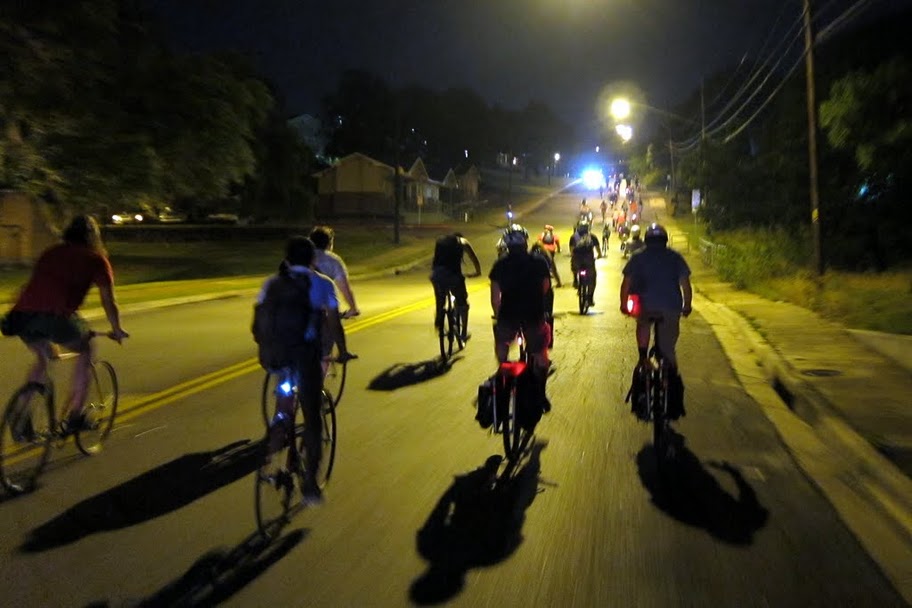 Rear view of cyclists, riding their bikes straight away, on a paved street under street lights at night