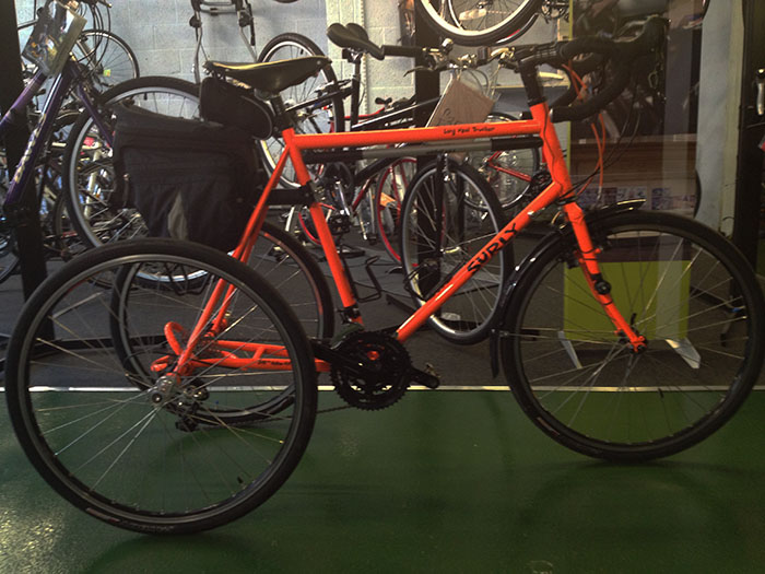 Right side view of a red, 3-wheeled, Surly Long Haul Trucker bike, parked inside a bike shop