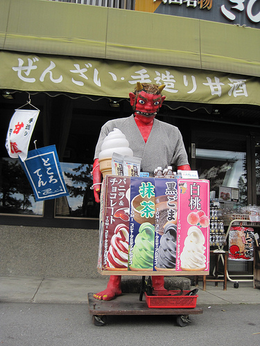 Front view of a demon mannequin, standing in front of an ice cream vending cart, on a street in front of a store