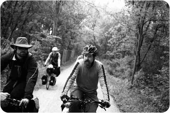 Front view of 2 cyclists, riding their bikes side by side, on a gravel road in the woods - black & white image