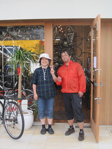 Front view of 2 people, side by side, in on open doorway of The Farm bike shop