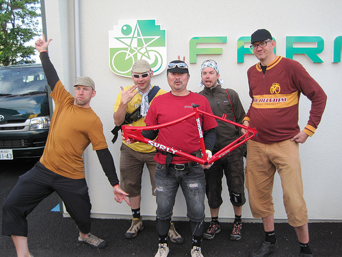 Front view of 5 people standing side by side, with the person in the middle holding up a red Surly Instigator bike frame