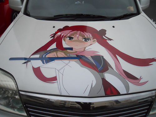 Downward, front end view of a car, with a painting of an anime child on the hood