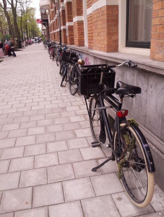 Rear, right side view of bikes, lined up against the side of a brick building, on a stone block side walk
