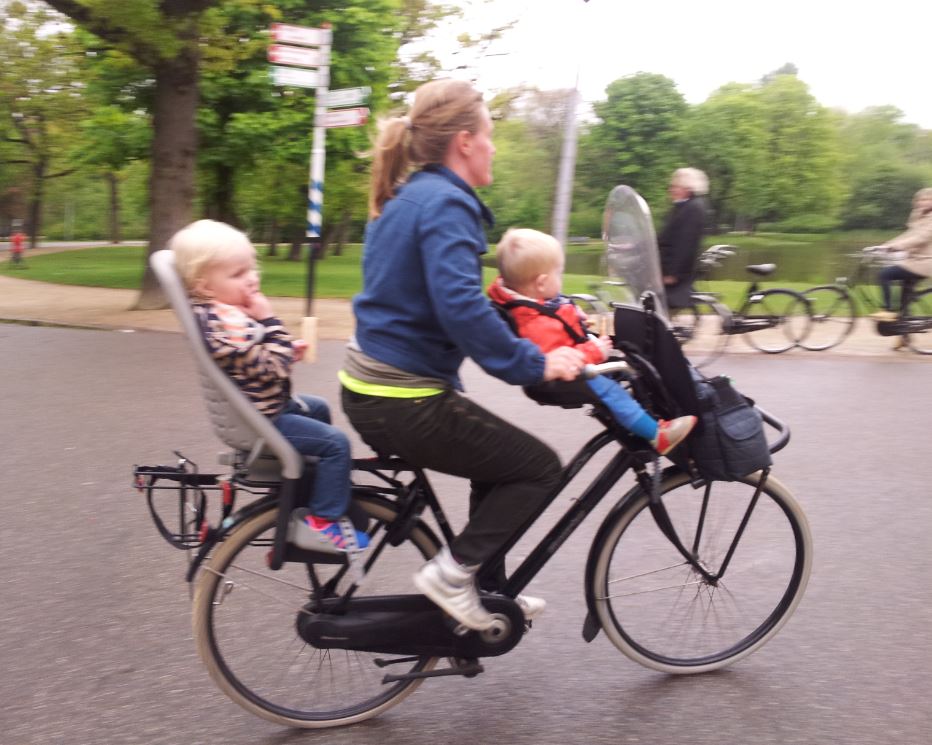 Right side view of a cyclist, riding a bike with children in bike seats on front and back