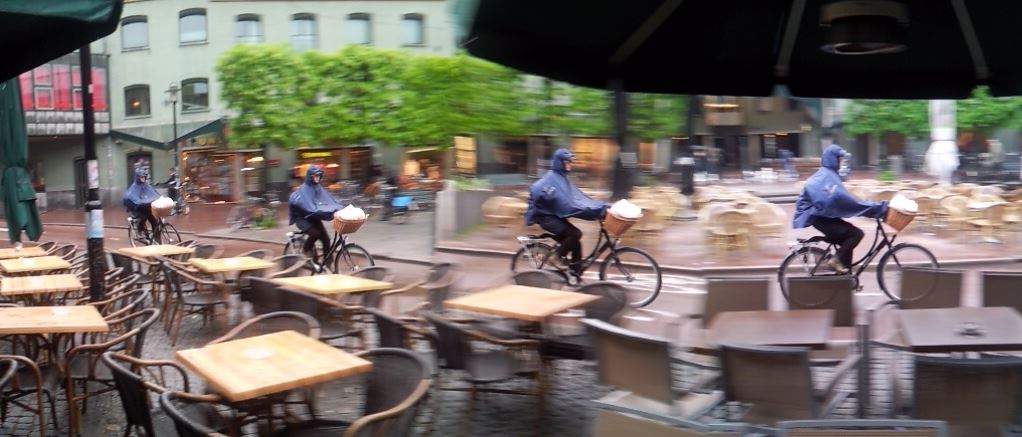 Right side time lapse image of a cyclist riding a bike in front of an outdoor cafe
