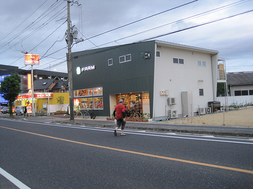 Rear view of a person crossing a city street, walking towards, The Farm, bike shop building