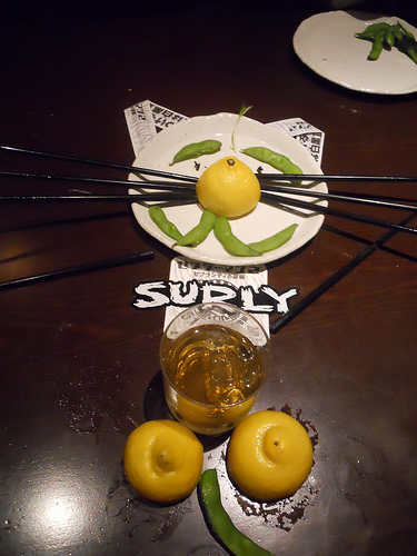 Downward view of a whiskey glass, with a Surly sticker laying above, on a table with items positioned to look like cat