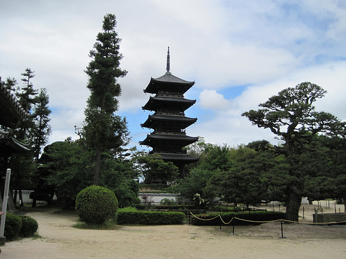 A 5 story Japanese pagoda, in the center of garden with hedges and trees, with blue sky and white clouds above