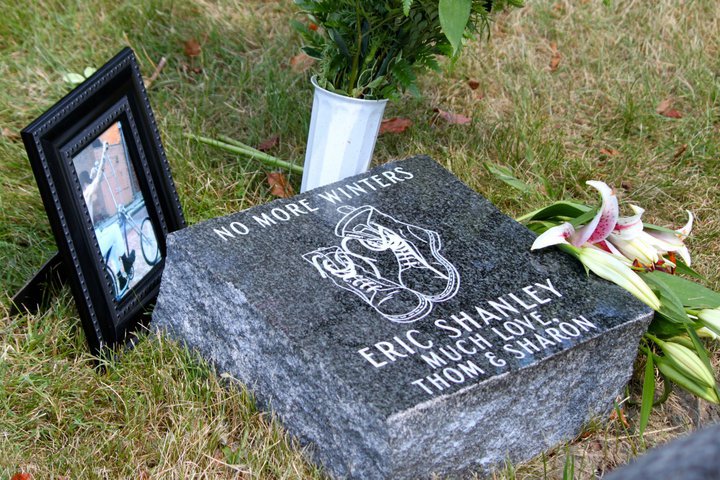 A granite grave plot stone on grass, with a picture frame and flowers next to it