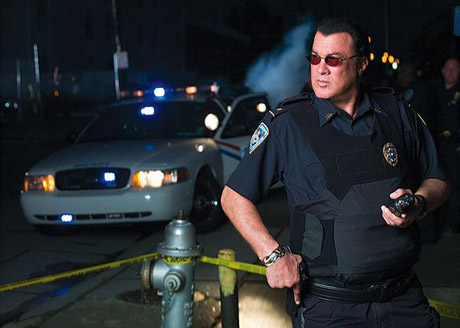 Screenshot of a movie screen, featuring the actor Steven Seagal, dressed in a police uniform on a sidewalk at night