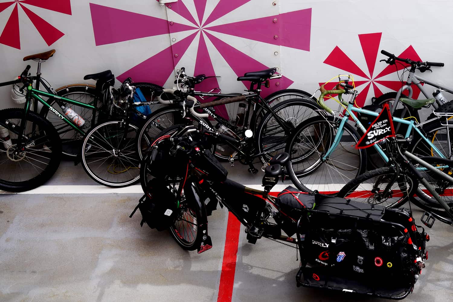 Many Surly bikes parked or leaning against each other and wall with pained designs