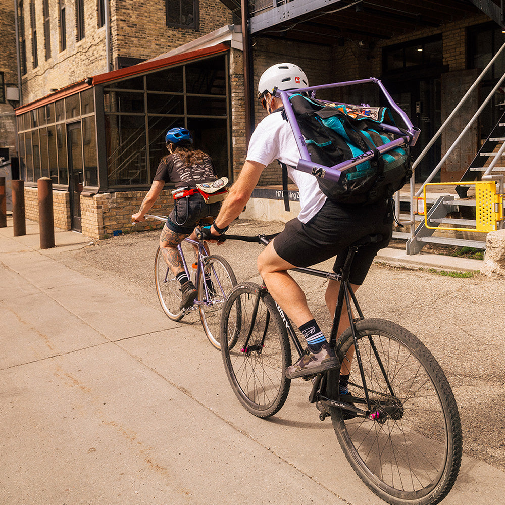 Two cyclist riding down an ally one with messenger bag with frame strapped to it