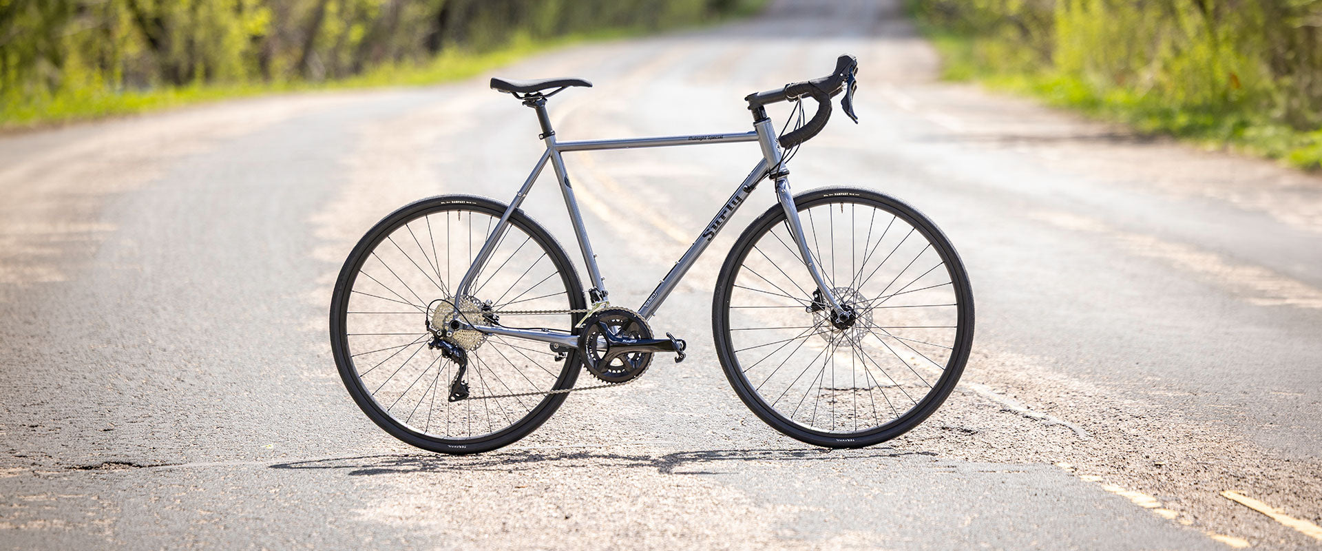 Gray bicycle on a paved road with greenery in the background