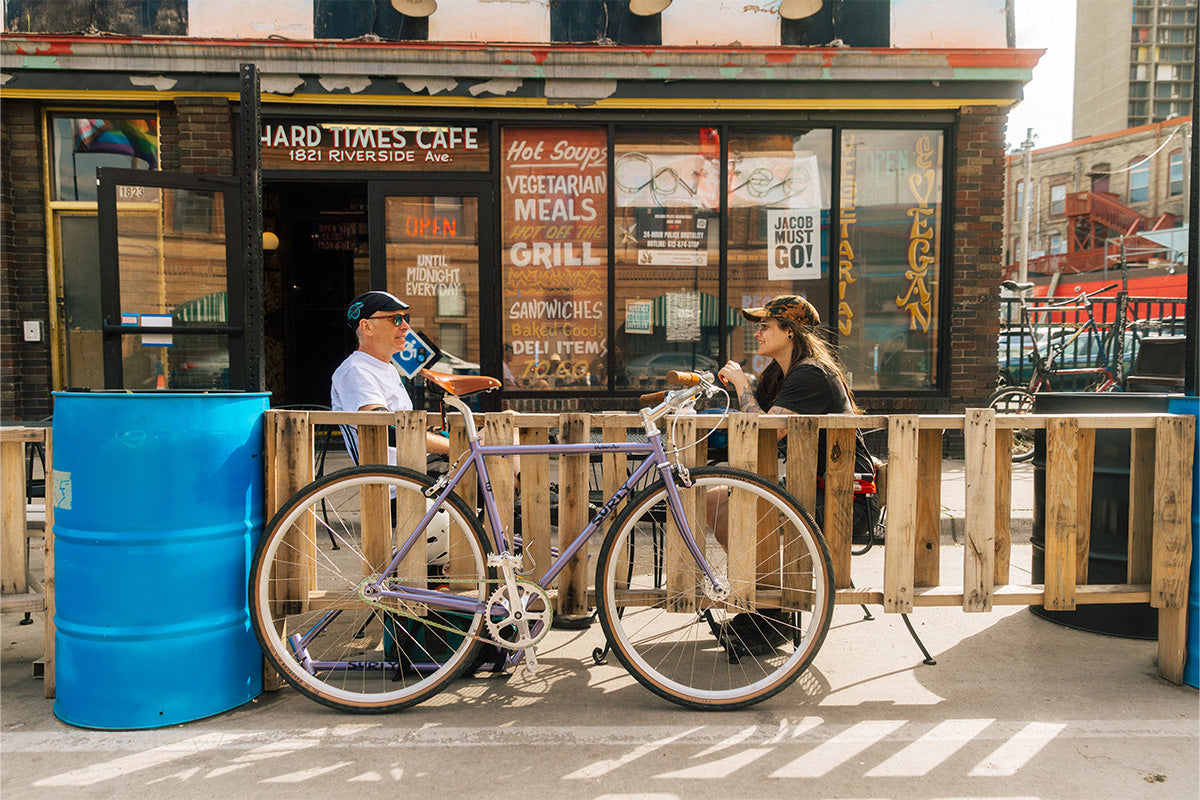 Two people sitting on a wooden bench with a Steamroller in front of a cafe.