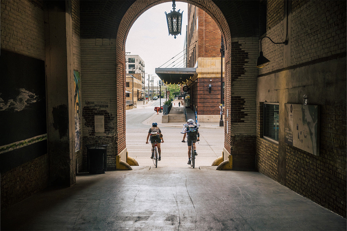 Two cyclists riding through an archway in an urban setting