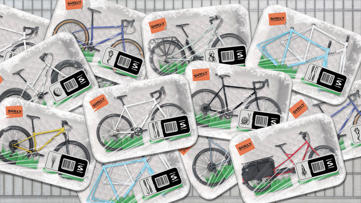 A close-up, top-down view of multiple packaged bicycle frames arranged on a gray grid surface. Each package contains a bicycle frame, with visible color options including white, black, yellow, blue, red, and light blue.