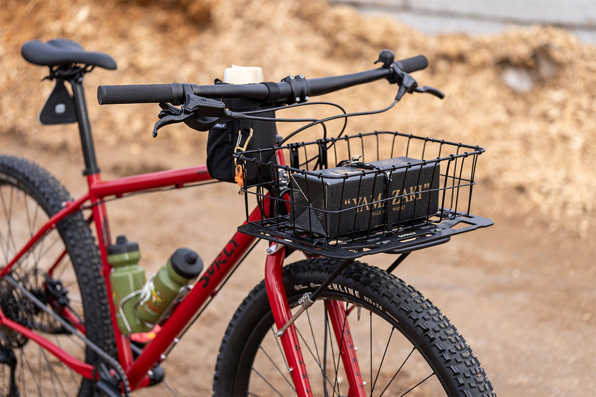 Red bicycle with a black basket and water bottles on a blurred natural background