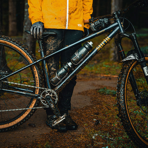 Person in yellow jacket standing next to a mountain bike on a trail