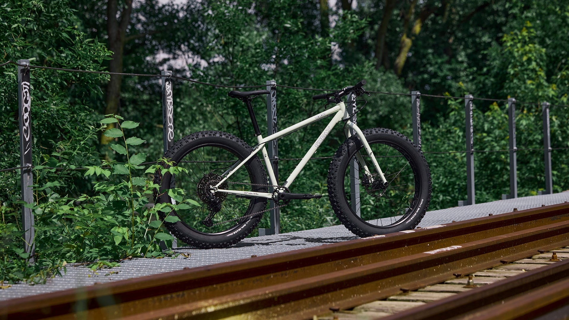 Surly Wednesday Fat Bike  leaning against a fence on a railway track with greenery in the background