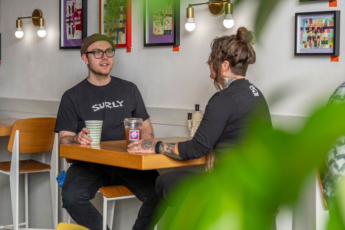 Two people sitting at a table in a casual setting with 'Surly' shirts on.