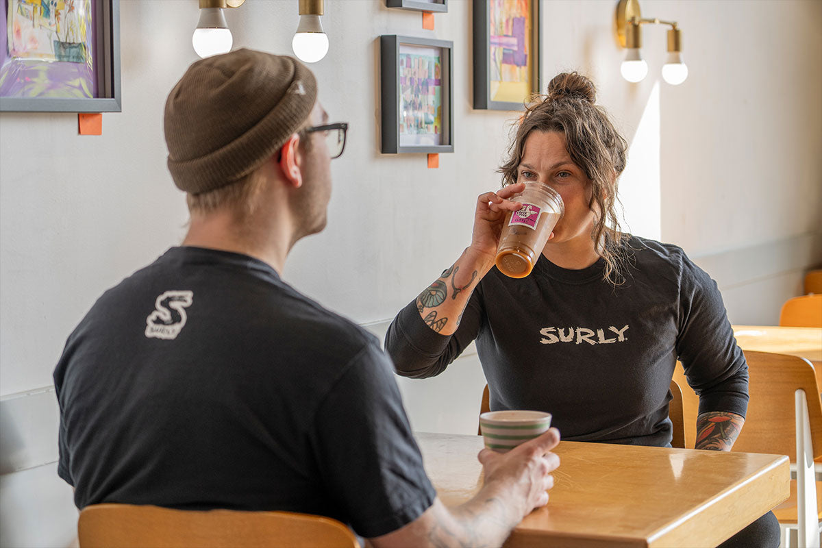 Two people sitting at a table in a casual setting, one drinking from a cup.