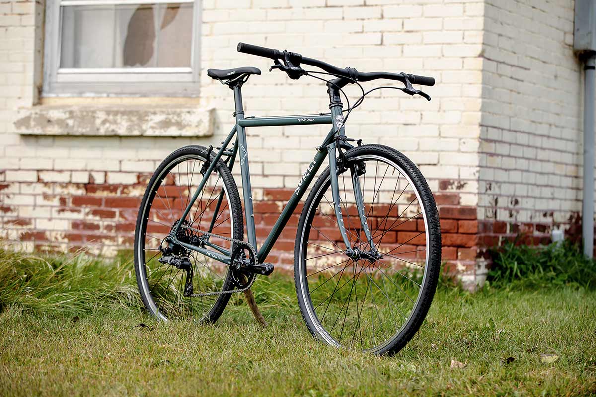 Cross-Check BlueGreenGray complete bike three-quarter front view propped up with stick on grass next to brick building