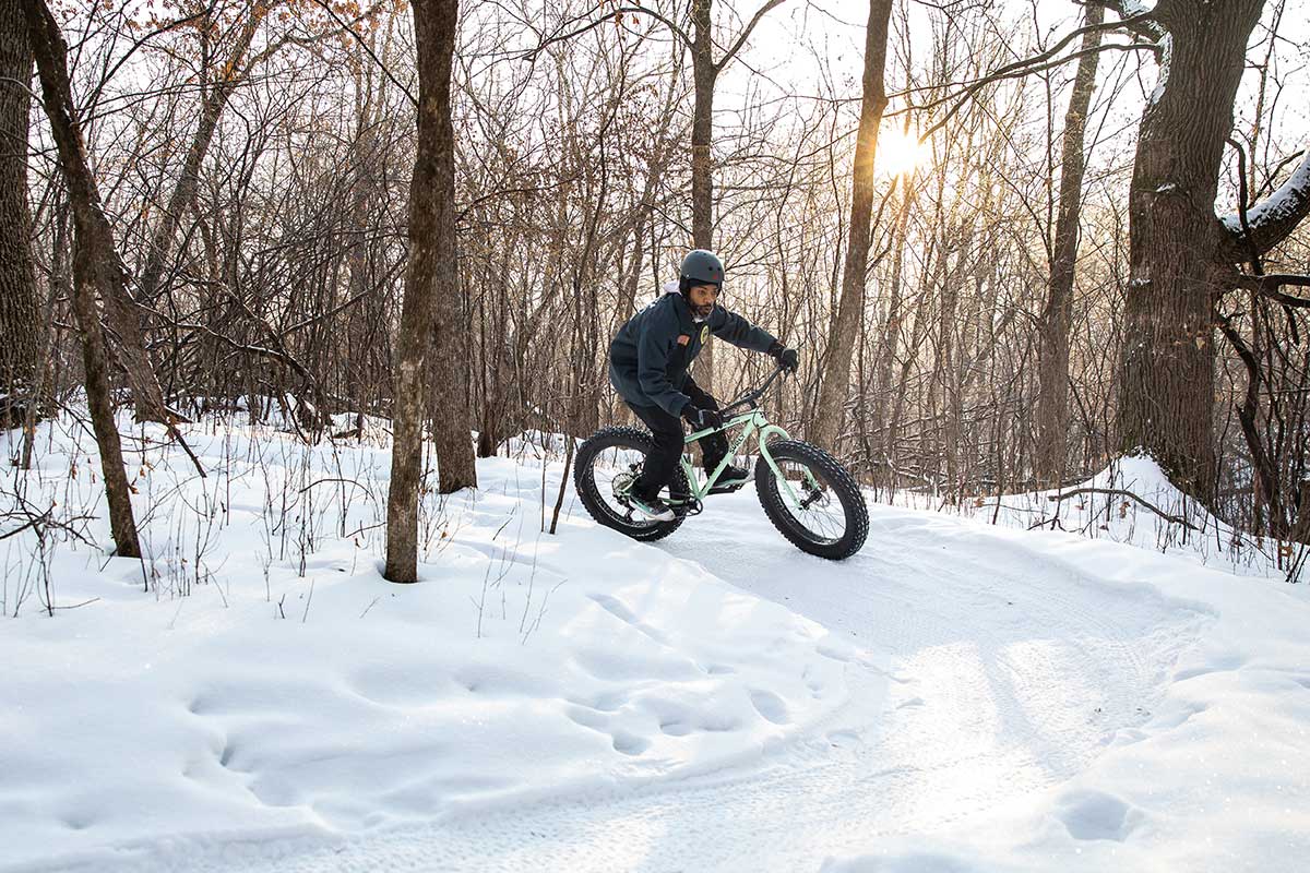 Person riding Ice Cream Truck bike on snow trail in winter, going around corner in woods