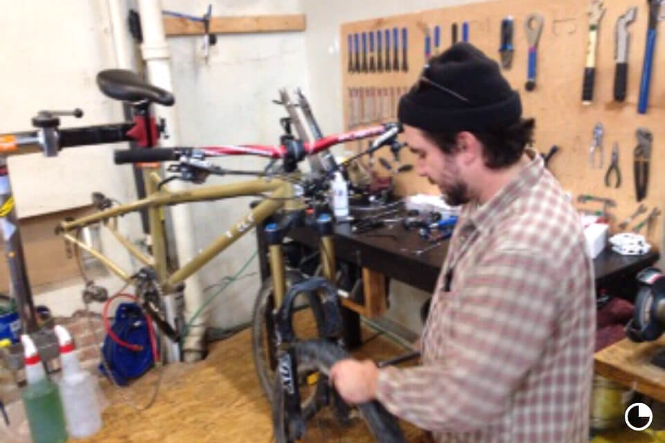 A person wearing a black stocking cap, putting a fender on a bike fork, in a workshop