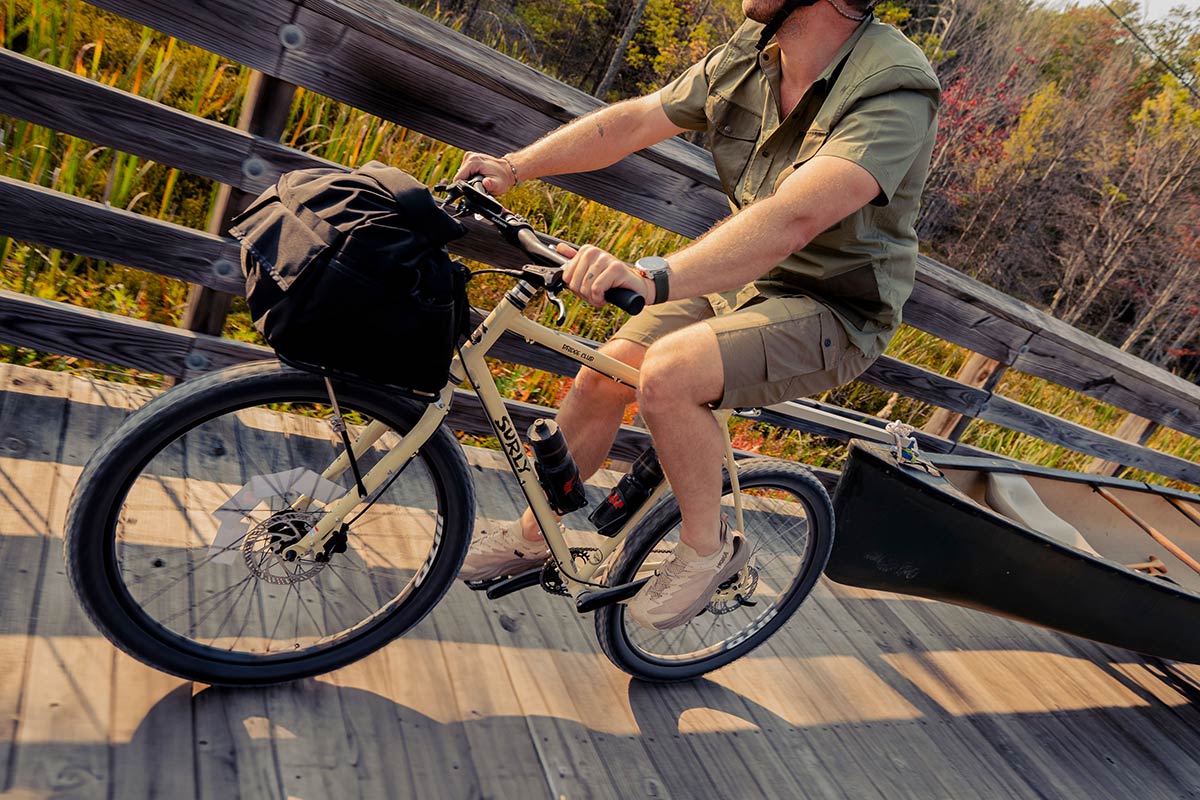 Cyclists riding Surly Bridge Club bike towing canoe over wooden bridge