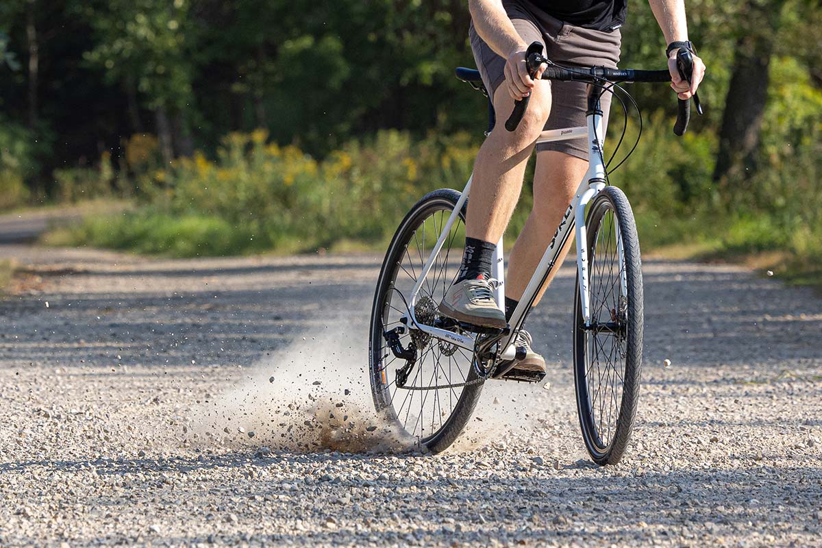 Person riding Surly Preamble Drop Bar Thorfrost White bike skidding rear wheel on gravel road focus on bike