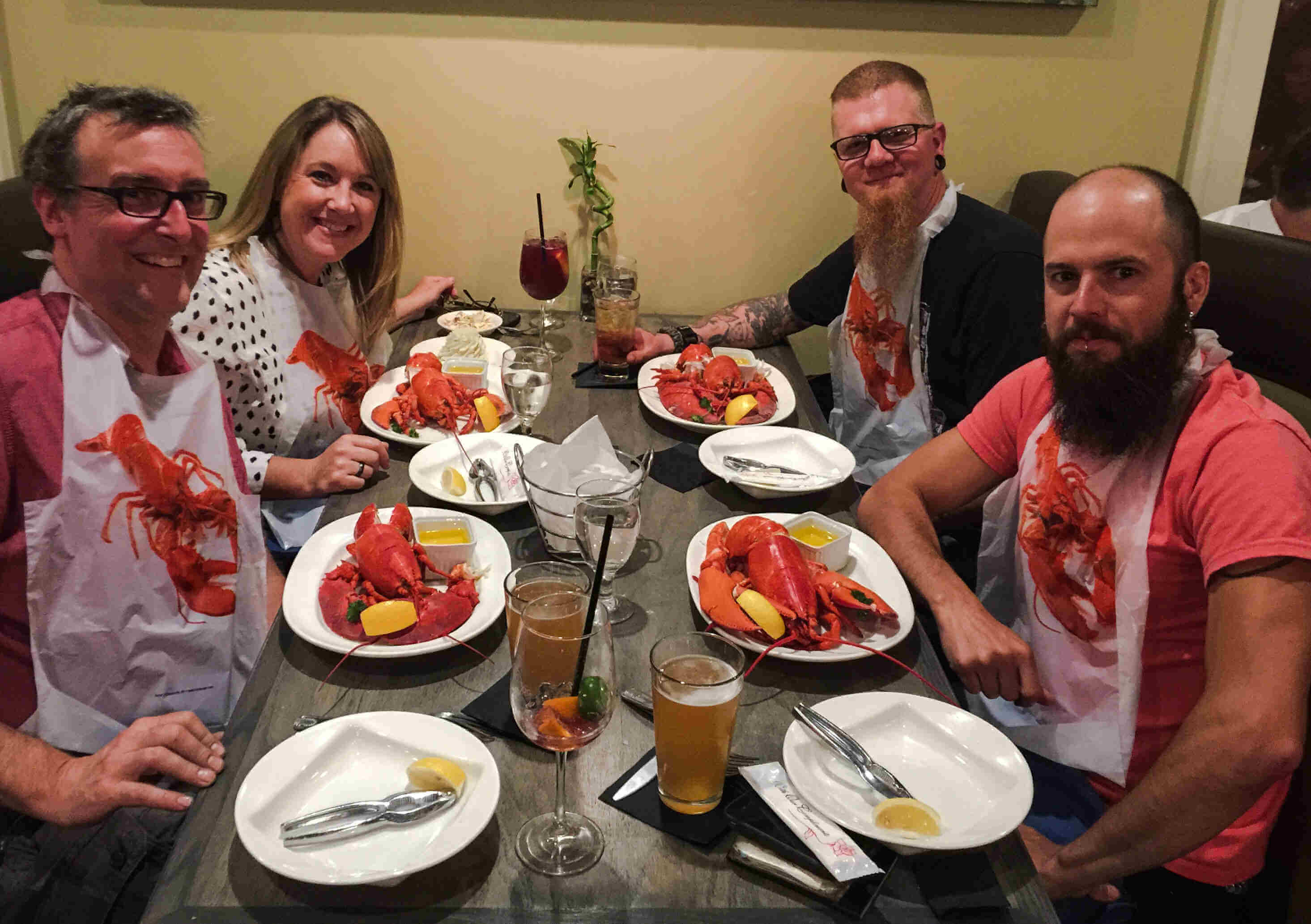 Four people sitting at a table, posing with plates of lobsters in front of them