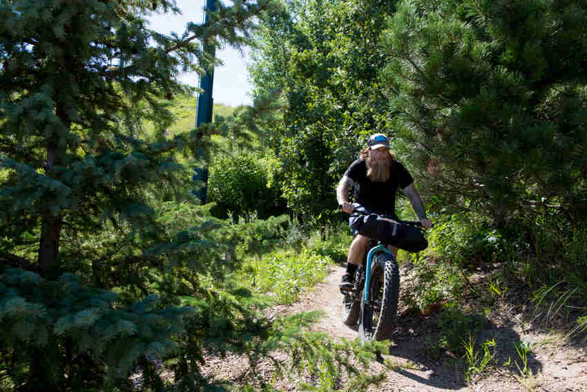 Front view of a cyclist, riding a fat bike with a front pack, down a dirt trail in the forest