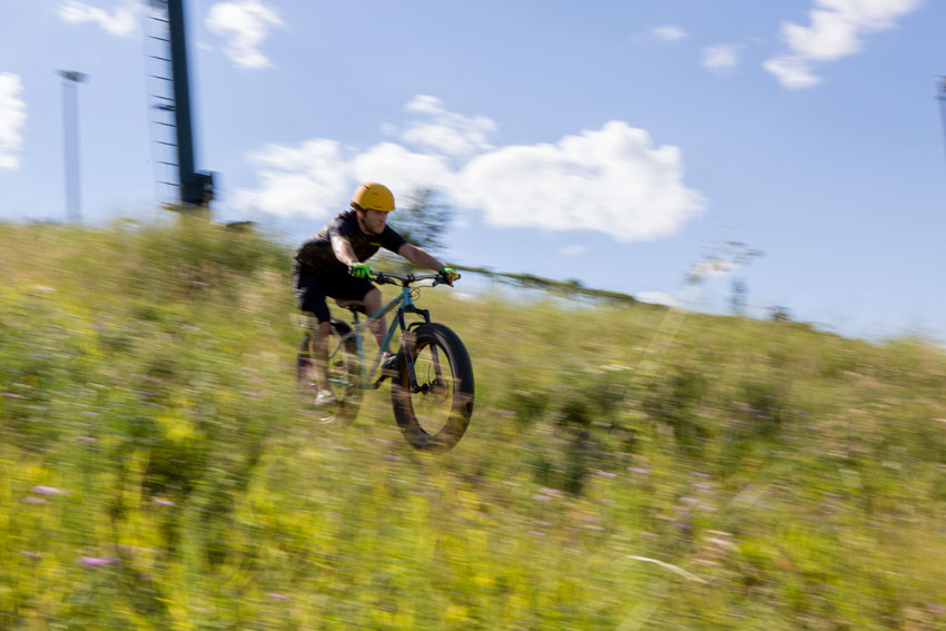 Front, right side view of a cyclist, riding a fat bike, speeding down a grassy hill