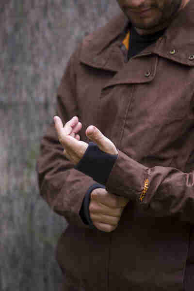 Front close up view of a person wearing a Surly V2 Waxed canvass jacket, brown, featuring the handwarmer cuffs