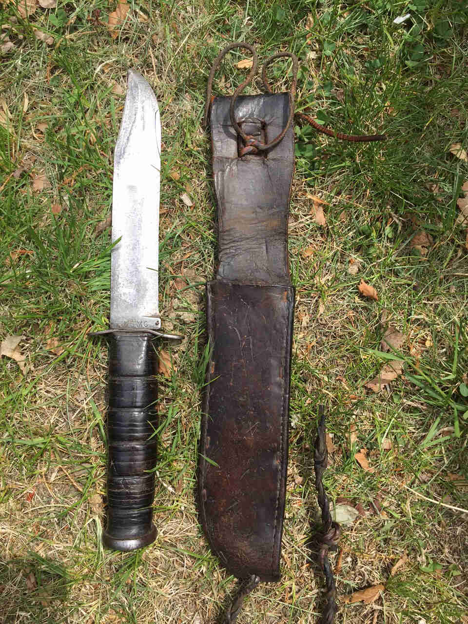 Downward view of a fixed blade knife and sheath, laying on grass