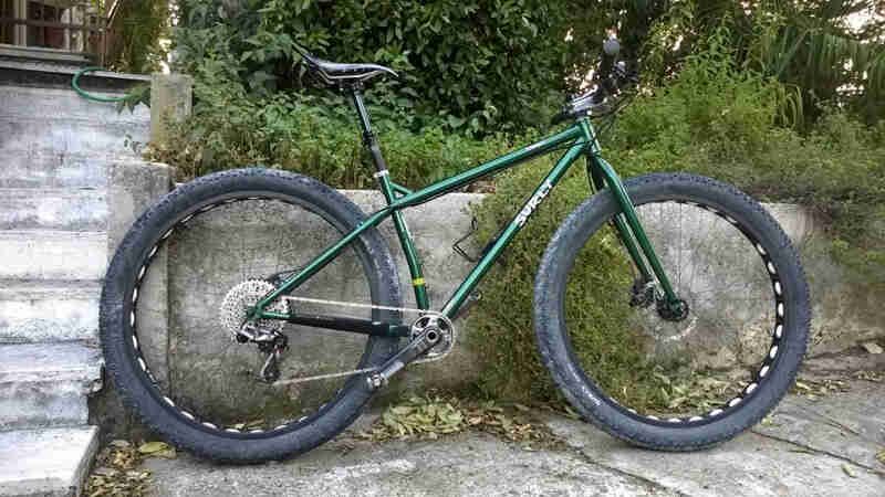 Right side view of a green Surly bike, parked against a cement wall, next to a set up stairs