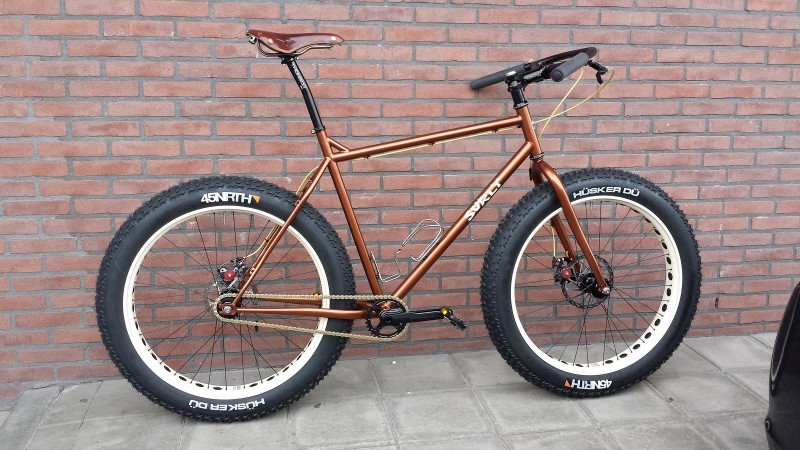 Right side view of a copper Surly fat bike with white rims, leaning against a brick wall on a sidewalk
