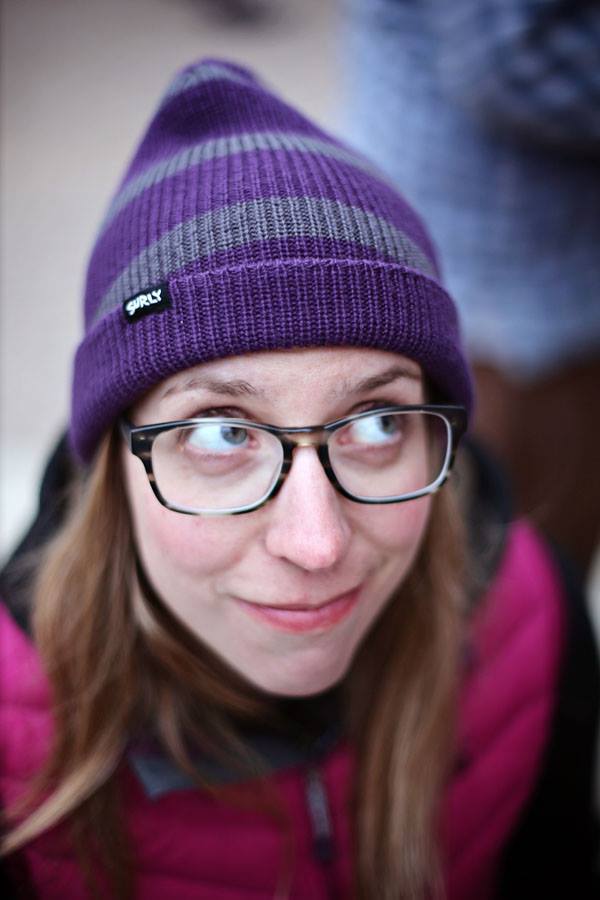 Headshot of a person wearing a purple and gray Surly stocking cap and glasses, with their eyes looking up