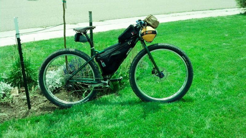 Right side view of a green Surly bike loaded with gear, parked in the grass of a front yard, next to a landscape plot