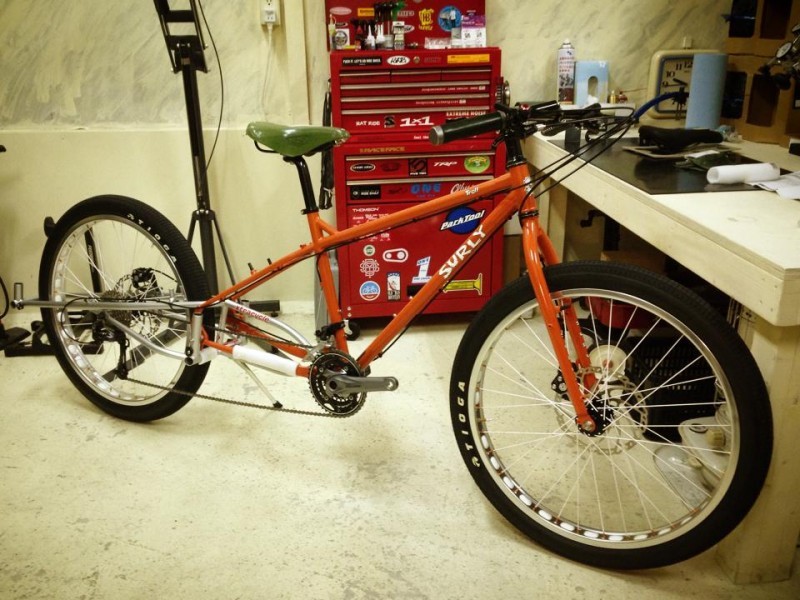 Right side view of a modified, orange Surly bike, in a workshop with a tall, red tool chest