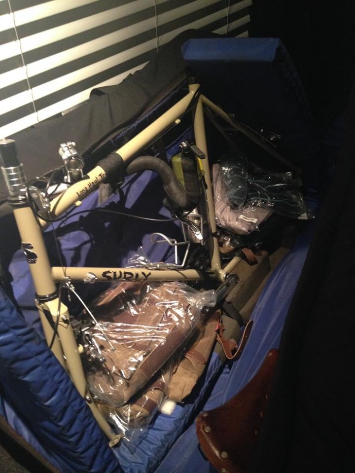 Left side view of a disassembled, tan Surly Long Haul Trucker bike, packed in an unzipped bike carrier bag