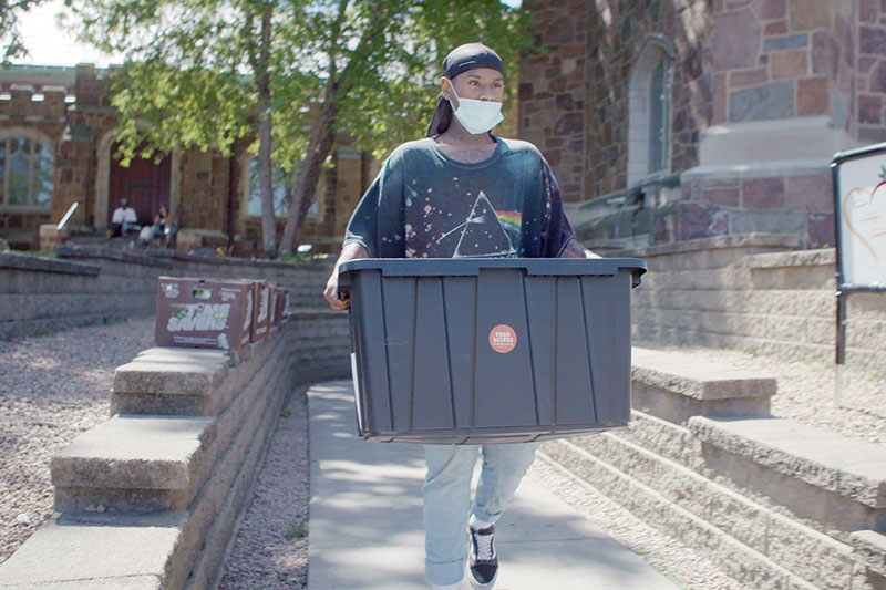 Person carrying large bin of food to building, walking on sidewalk