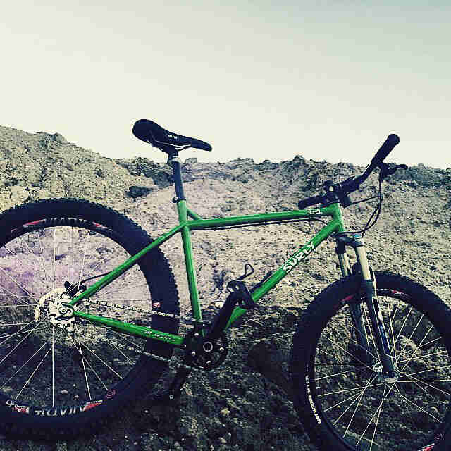 Right side view of a green Surly 1x1 bike, parked against a dirt mound